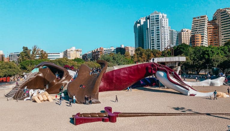 A large playground structure in Valencia shaped like the character Gulliver, where children can climb and slide down the giant figure. The whimsical design stands against a backdrop of modern buildings, offering a unique play space.