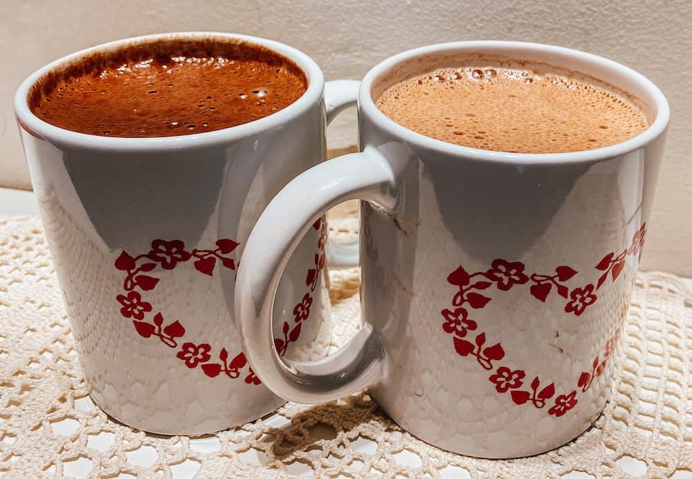 two cups of vegan hot chocolate in mugs with a heart on it