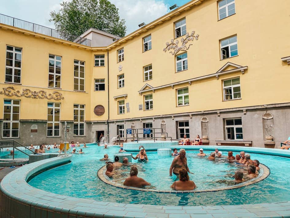 Outdoor pool with people inside in a courtyard of a yellow house in Budapest