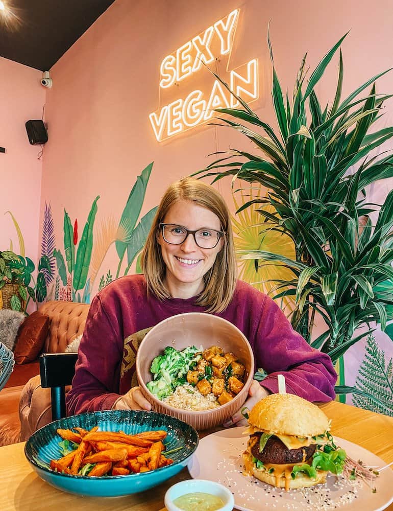 A woman holding a bowl of food with more food on the table at one of the best vegan restaurants Belgrade has to offer