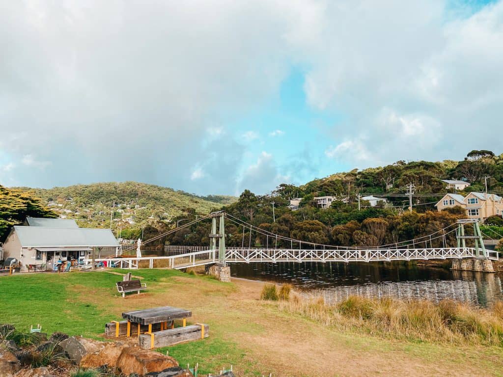 A small pedestrian bridge over a river, on one side is a café on the other you can only see nature