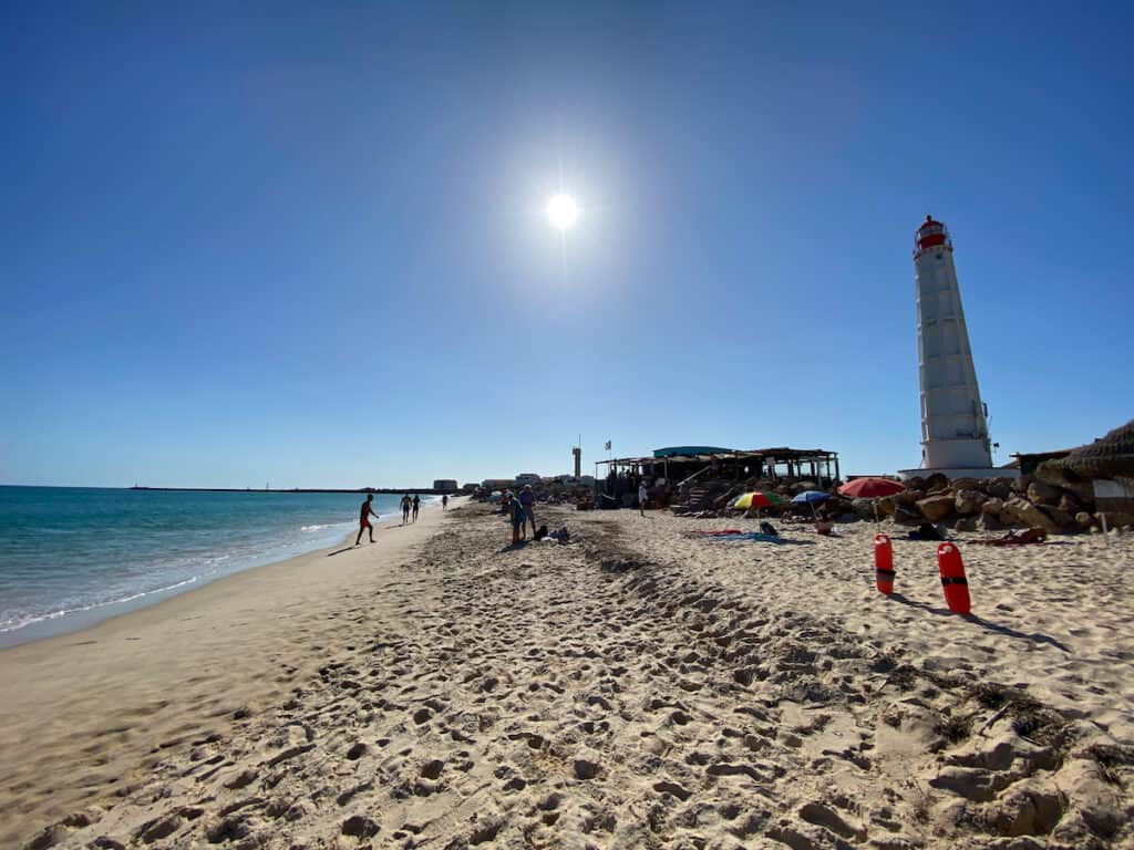 A lighthouse next to a beach with people on it, very relaxed beach at Ilha do Farol