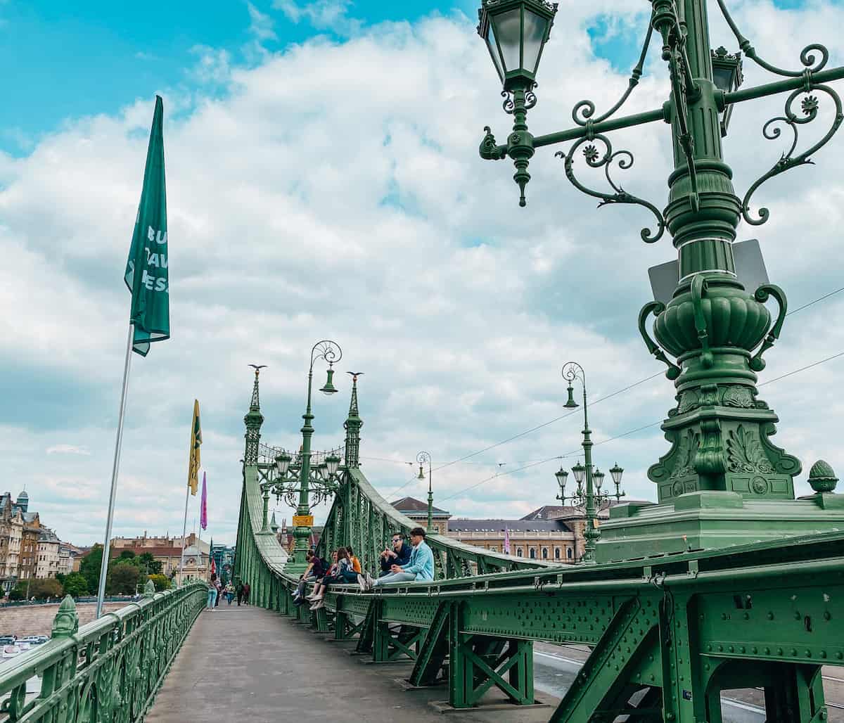 The pedestrian walkway on a busy bridge, with people sitting on the railing