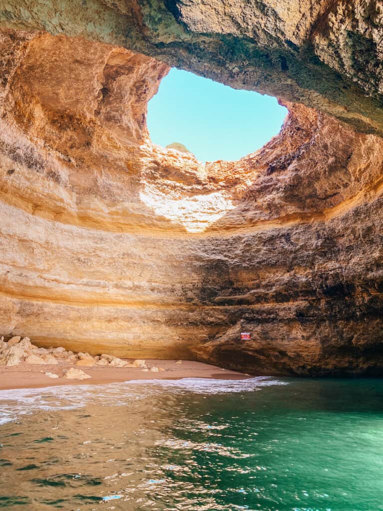 A cave with a circular opening at the top and green water at the bottom; those are the famous Benagil caves in the Algarve
