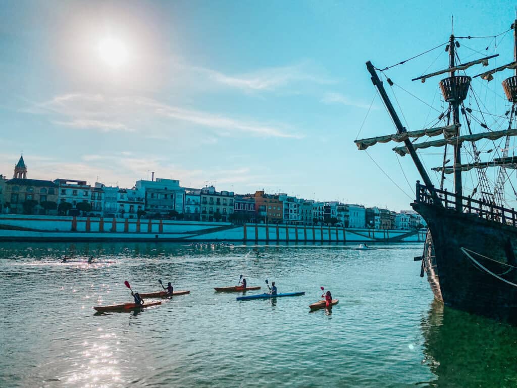Kayaks on a river going past a big, historic ship