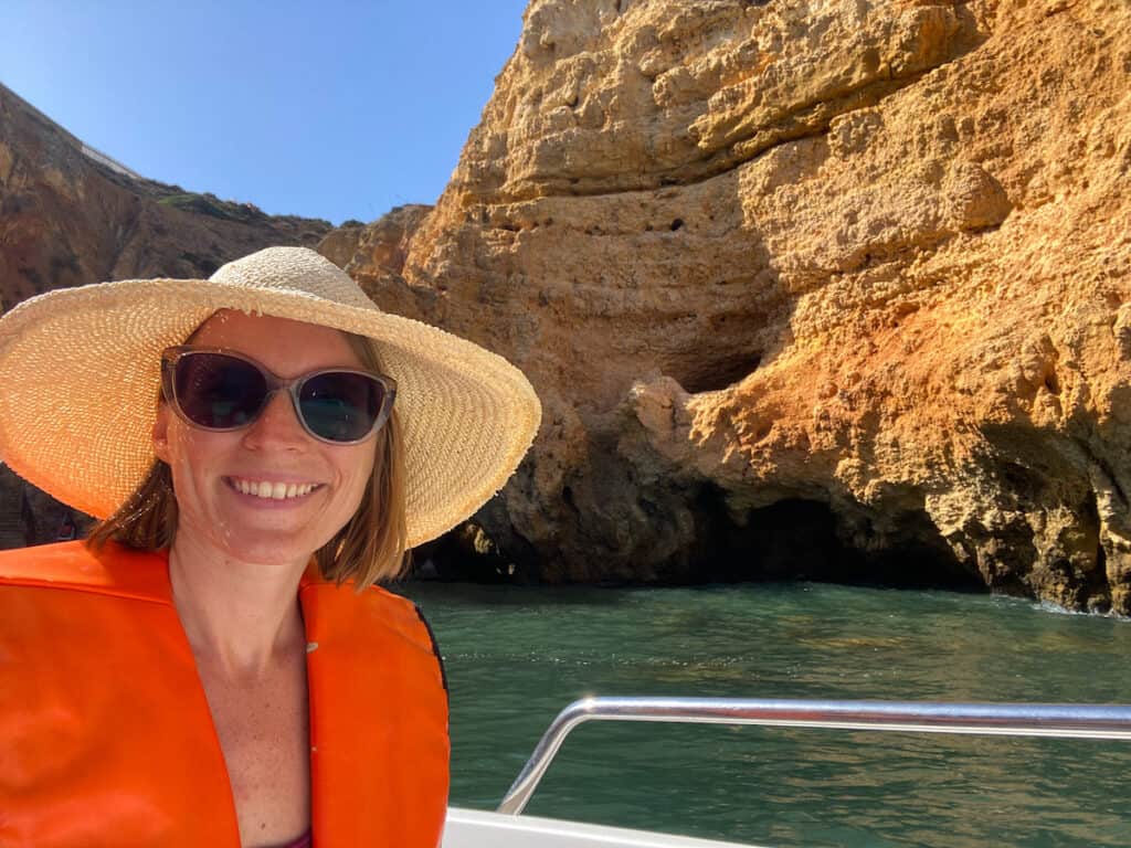 Tina in a boat with a straw hat, in the back are impressive cliffs; a boat tour is one of the best things to do in Lagos Portugal