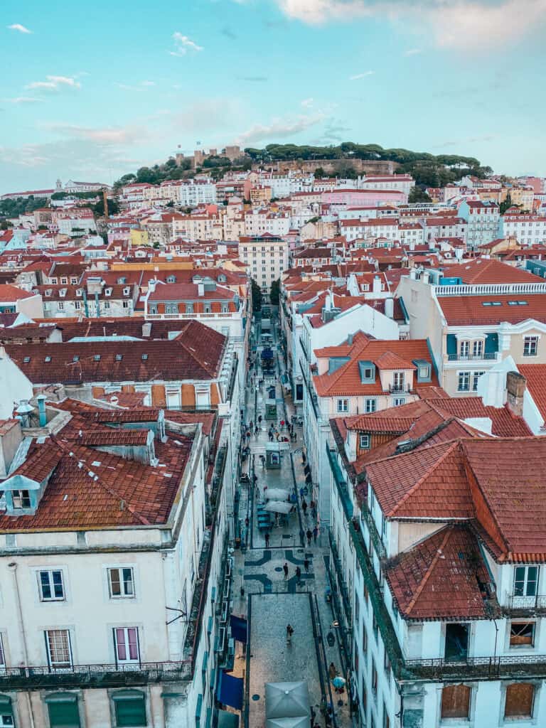Aerial view of a bustling street in Lisbon, with terracotta rooftops stretching towards the historic castle on the hill, capturing the essence of things to do in Lisbon on a Spain and Portugal itinerary.