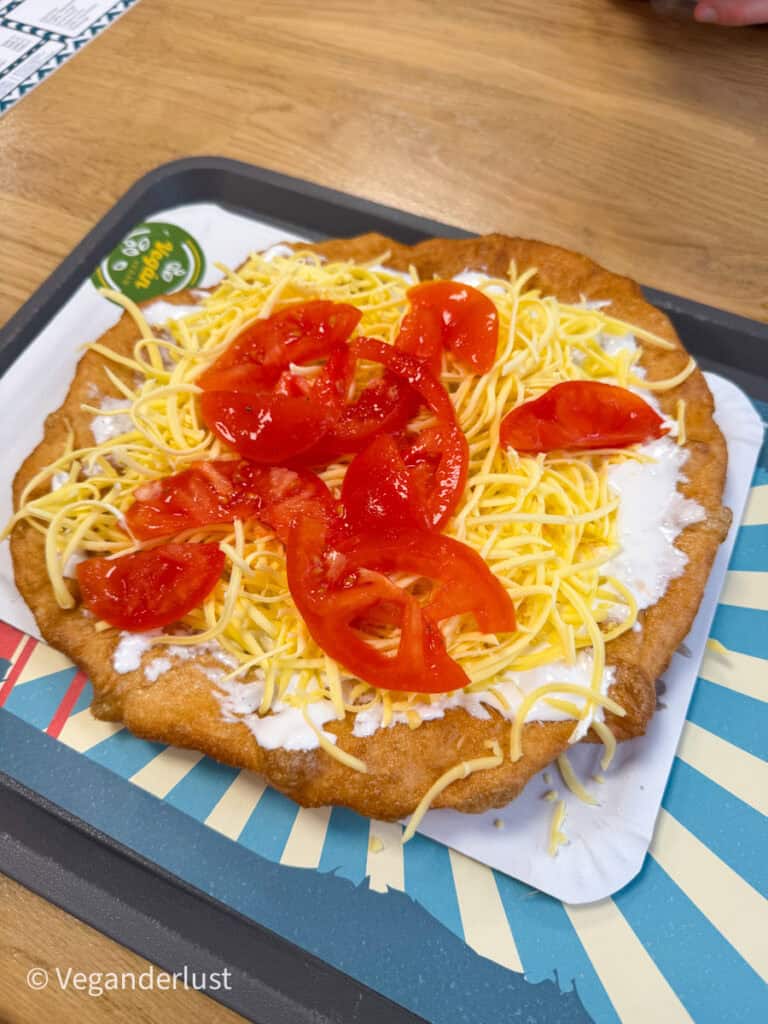 Fried flatbread topped with a layer of white sauce, shredded yellow cheese, and fresh tomato slices served on a tray in a casual eatery.
