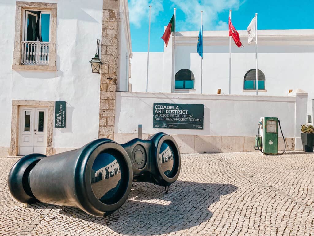 An oversized pair of binoculars in front of a white building with flags on it in Cascais