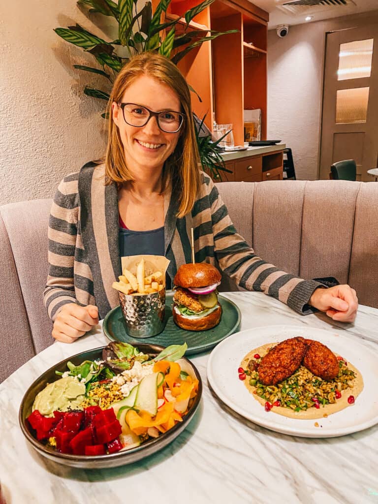 Tina sitting at a table with three different vegan dishes on it at a vegan restaurant in London, one of the top 10  most vegan friendly cities in Europe