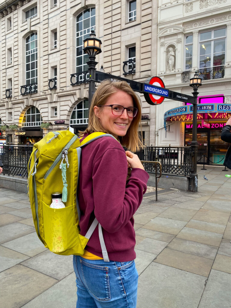 Tina wearing a Patagonia backpack in front of an underground sign in London, the post is about an honest Patagonia Black Hole 25l review