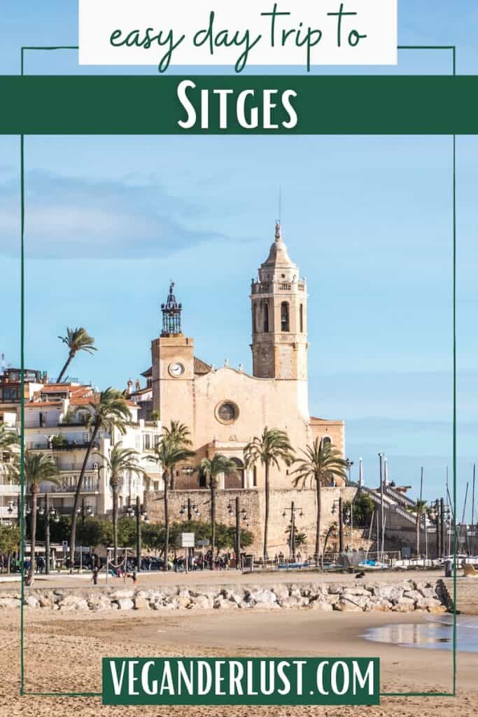 Sunny waterfront view of Sitges with a sandy beach. Palm trees and the Church of Sant Bartomeu and Santa Tecla overlooking the Mediterranean Sea. Text reads "easy day trip to SITGES" and "VEGANDERLUST.COM".