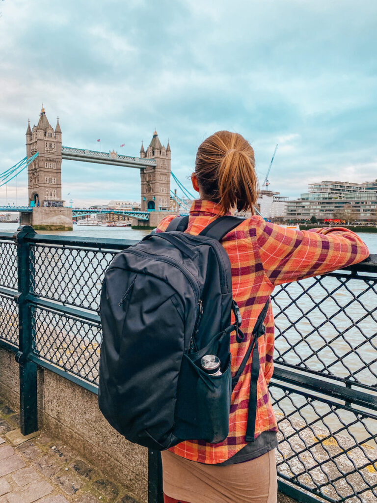 Tina wearing a Patagonia Refugio 26L backpack gazes at the Tower Bridge in London, demonstrating the backpack's comfort and style in a real-world setting for a Patagonia Refugio 26L review.