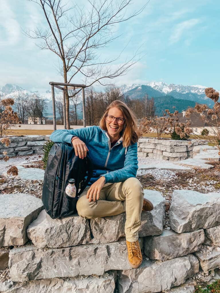 seated on stone steps with a Tortuga 30L travel backpack, showcasing the backpack's comfort and style against a mountainous backdrop.