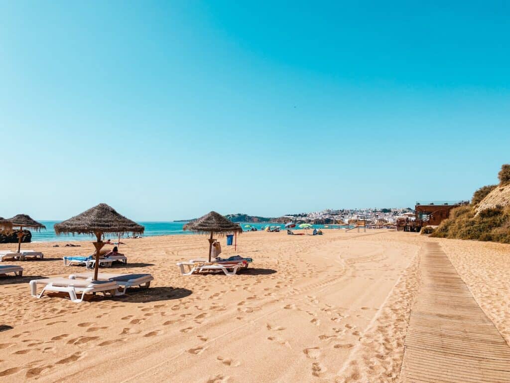 Sun-drenched Albufeira beach with straw umbrellas and loungers, inviting visitors to relax as one of the best things to do in Albufeira, Portugal.