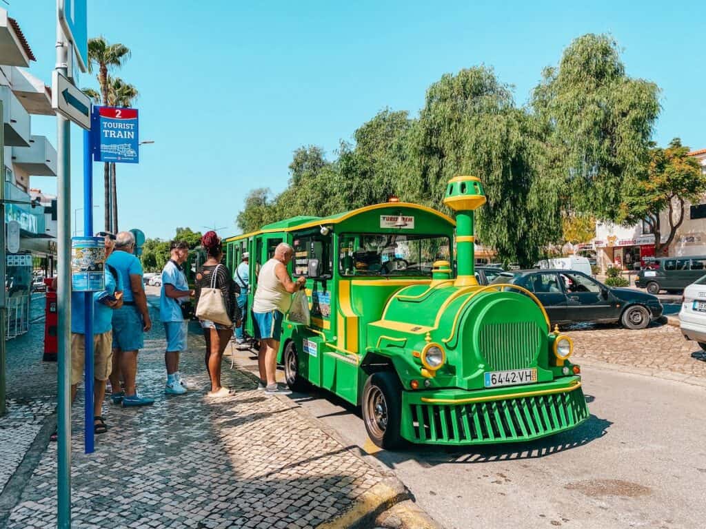 Tourists boarding the charming green tourist train in Albufeira, an enjoyable way to see the sights and a top attraction in Albufeira, Portugal.