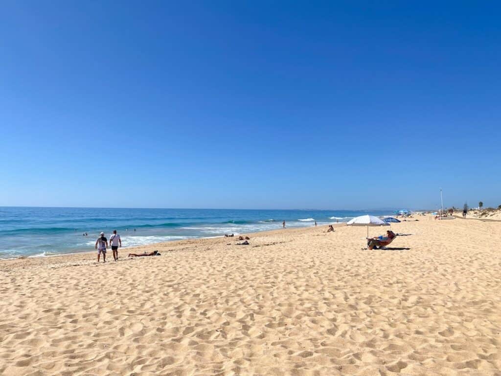 A serene beach setting in Faro with visitors enjoying the sun and sea, a prime example of the relaxing activities to enjoy while exploring things to do in Faro.