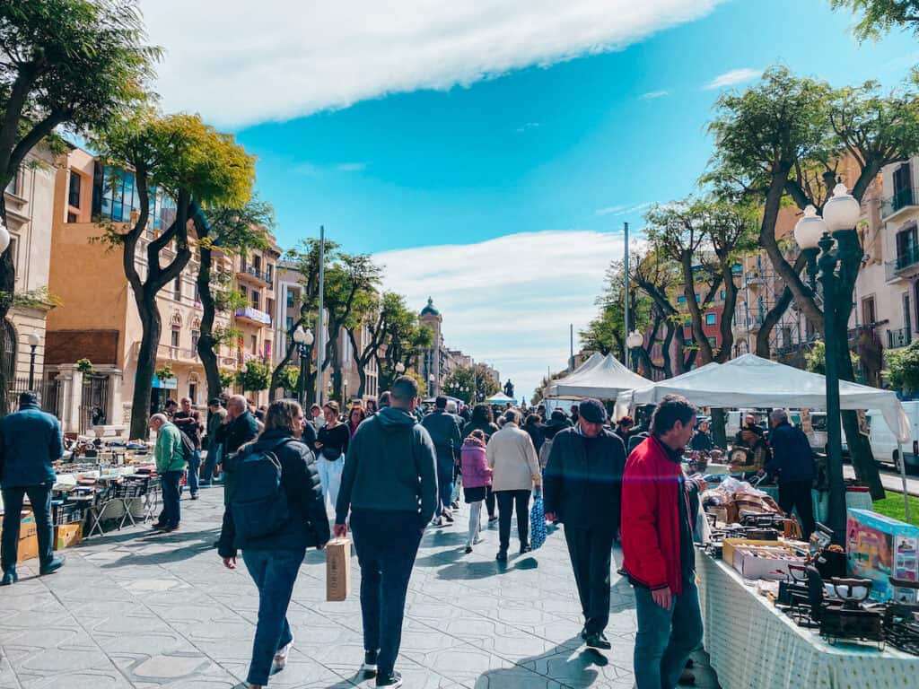 Shoppers and vendors fill the Rambla Nova in Tarragona during a lively street market, surrounded by the colorful facades of city buildings—a snapshot of local life and daily commerce.