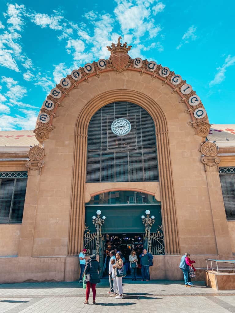 The bustling entrance of the Mercat Central de Tarragona, with visitors gathered around, a popular spot for experiencing local life and cuisine while exploring Tarragona Spain.
