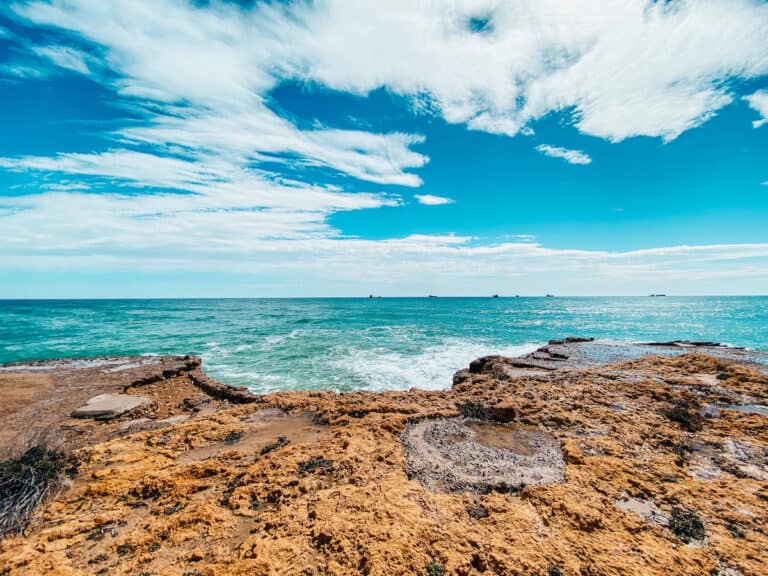 Crystal clear waters of the Mediterranean Sea against a rocky shoreline under a blue sky, a serene view for those enjoying coastal things to do in Tarragona Spain.