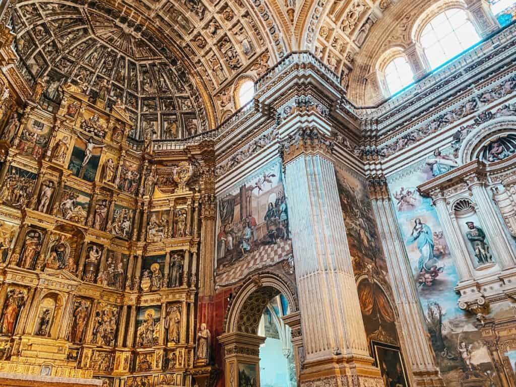 A historic church in Granada with an intricate altar and wall paintings next to it. 