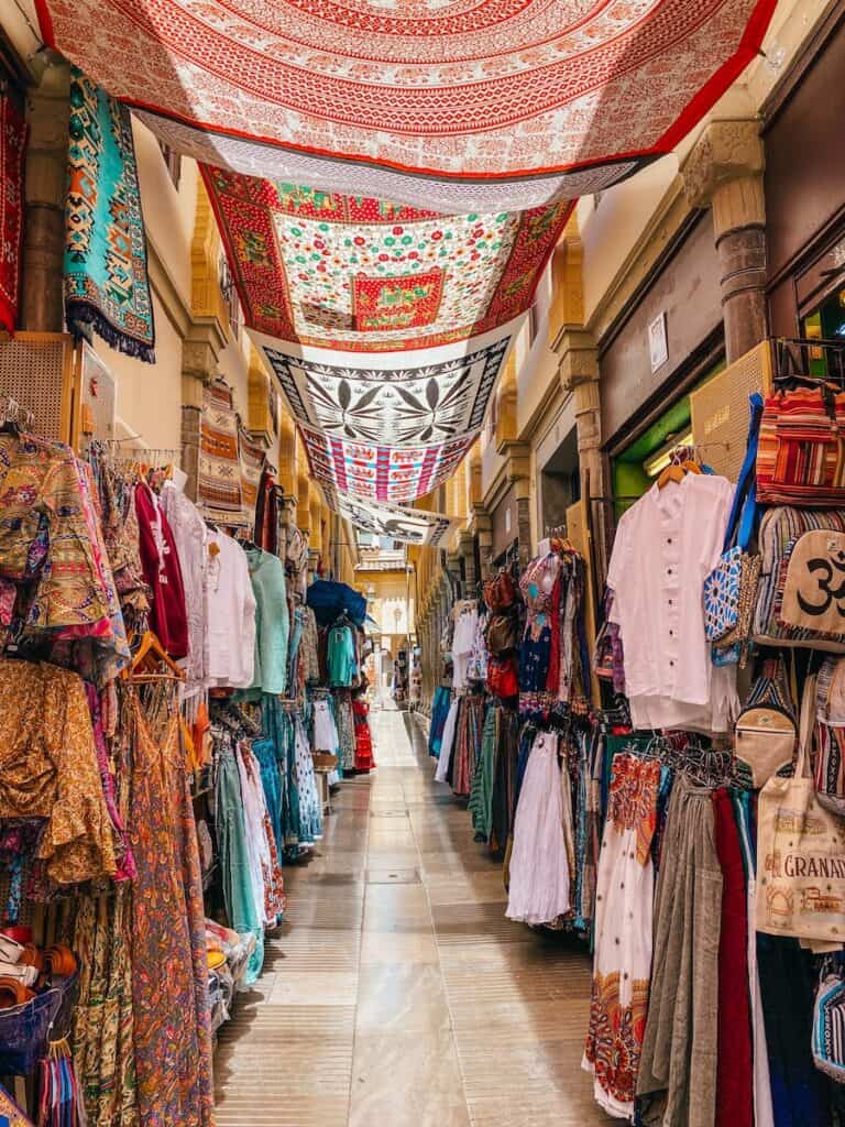 A colorful market in Granada, Spain, with vibrant textiles hanging overhead and stalls lined with traditional clothing and souvenirs.