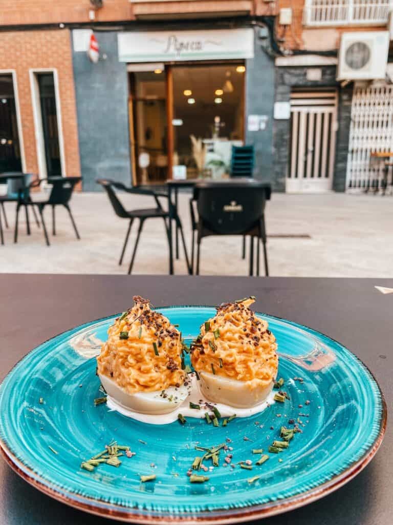 Two vegan devilled eggs on a blue plate, in the background you can see an outdoor sitting are at one of the vegan restaurants in Murcia.
