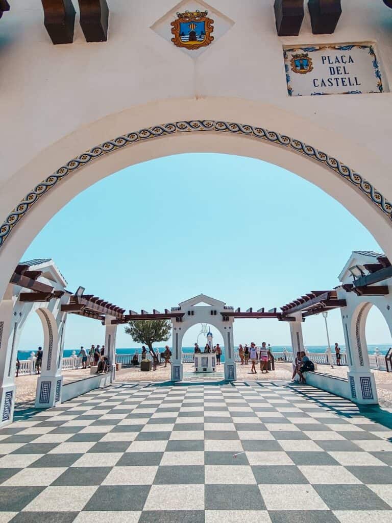 A square with arches around it and a checkers floor, you can also see a blue sky over the square.