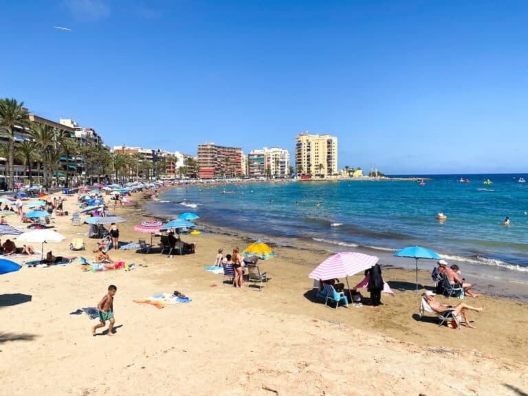 A vibrant beach in Torrevieja, Spain, with colorful umbrellas and people enjoying the sun, highlighting Torrevieja's top attractions.