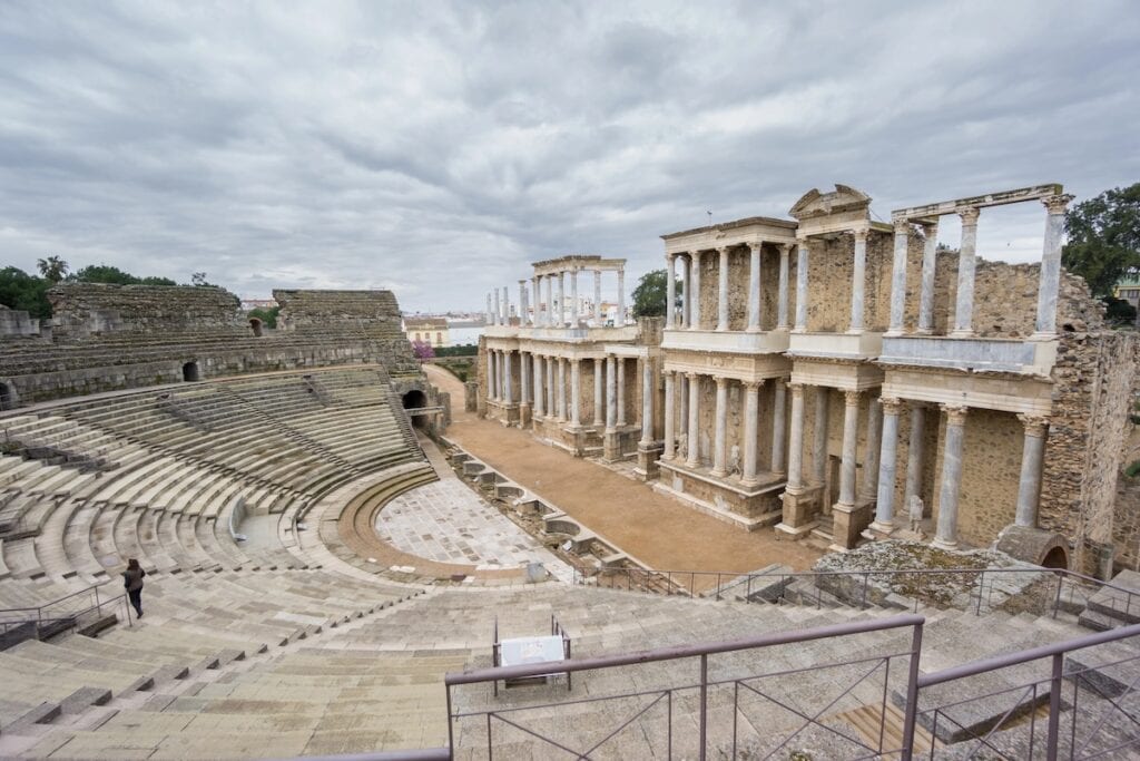 The ancient Roman Theatre in Mérida, Spain, showcasing its semicircular stone seating and well-preserved columns and arches. The cloudy sky adds a dramatic atmosphere to this iconic archaeological site.