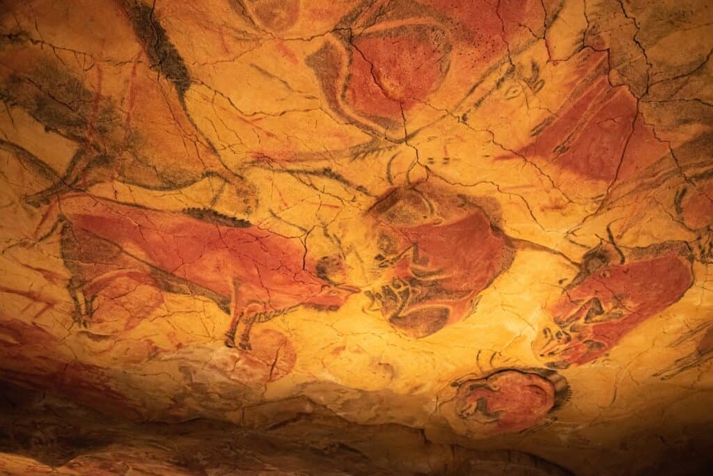 A close-up of prehistoric cave paintings from the Cave of Altamira, showcasing vivid depictions of bison and other animals in earthy red and brown tones. The cracked stone surface emphasizes the ancient artistry.