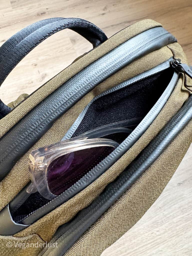 Top zipper pocket of the Alpaka Elements Pro Backpack partially open, revealing stored sunglasses, highlighting its convenient quick-access storage.