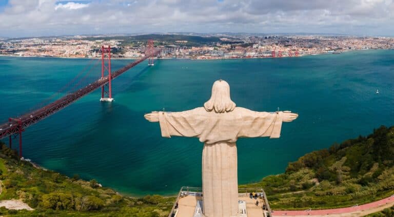 Aerial view of Sanctuary of Christ the King, Santuario de Cristo Rei. Lisbon, Portugal. Drone photo at sunrise with the 25 de Abril Bridge in background