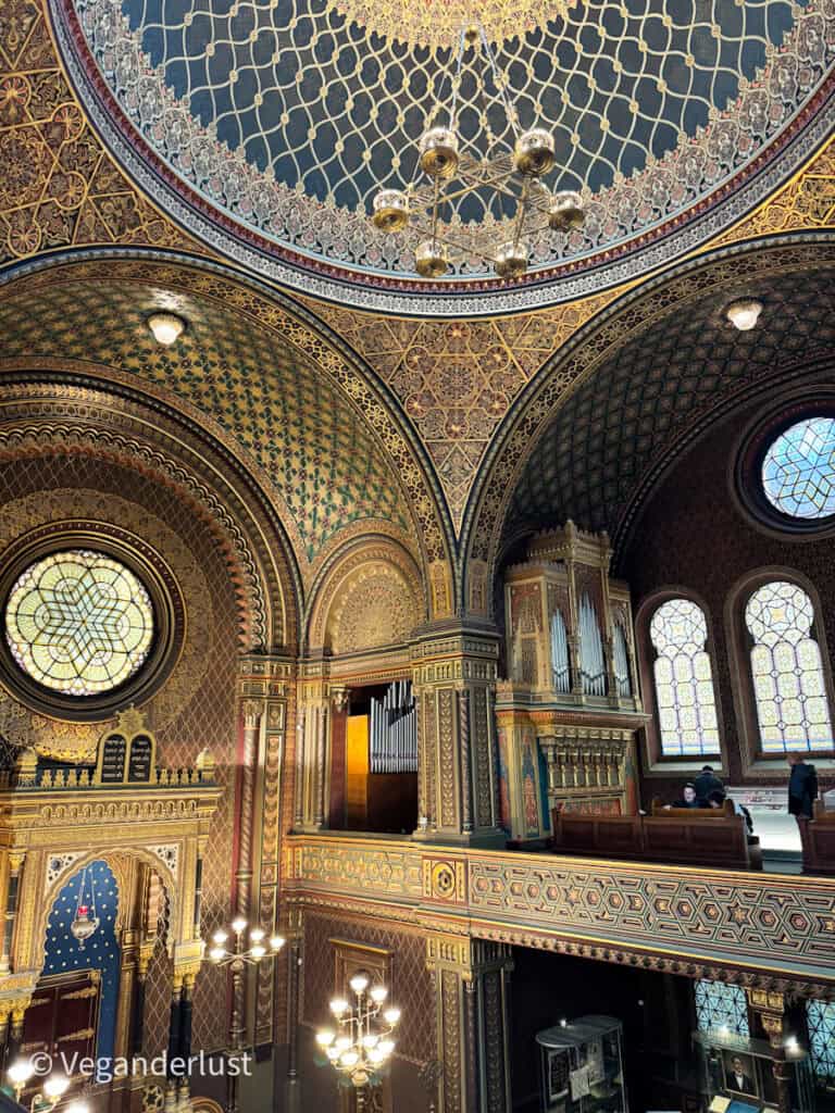 A stunning shot of the Spanish Synagogue’s richly decorated interior, with its domed ceiling, ornate arches, golden patterns, and stained glass windows glowing in natural light.
