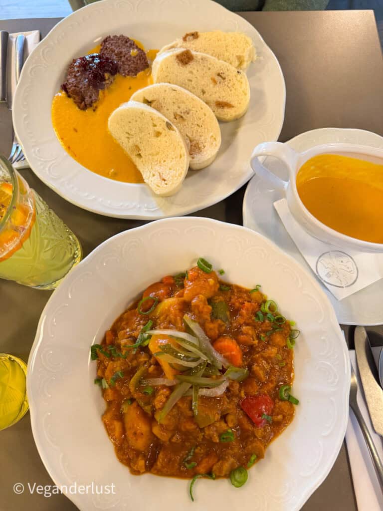 Two classic Czech dishes with a vegan twist: a hearty vegetable goulash with potatoes and scallions, and a plate of creamy svíčková sauce with dumplings and seitan medallions, served with a side of extra sauce in a gravy boat.