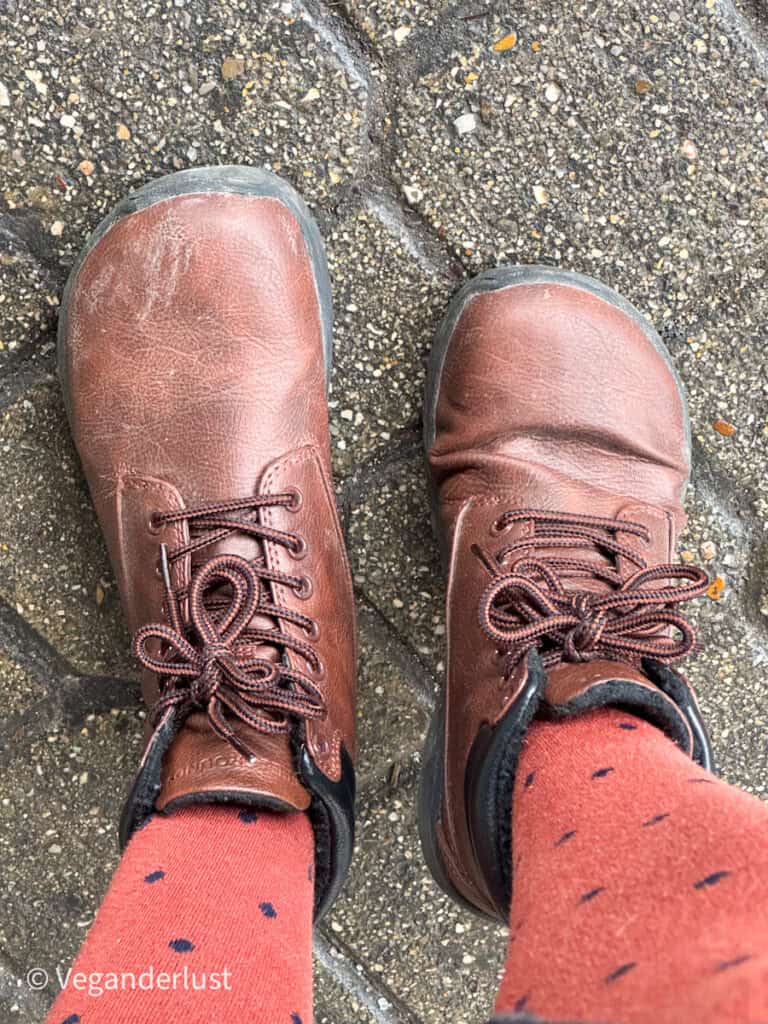 Top-down view of worn Feelgrounds Patrol Winter boots on cobblestone pavement, paired with orange polka-dot socks, showing creases and signs of regular use.