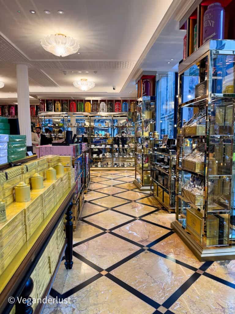Elegant TWG Tea boutique interior with glossy marble floors and glass cabinets filled with colorful tea tins. Chandeliers and mirrored shelves create a luxurious atmosphere for browsing premium teas.
