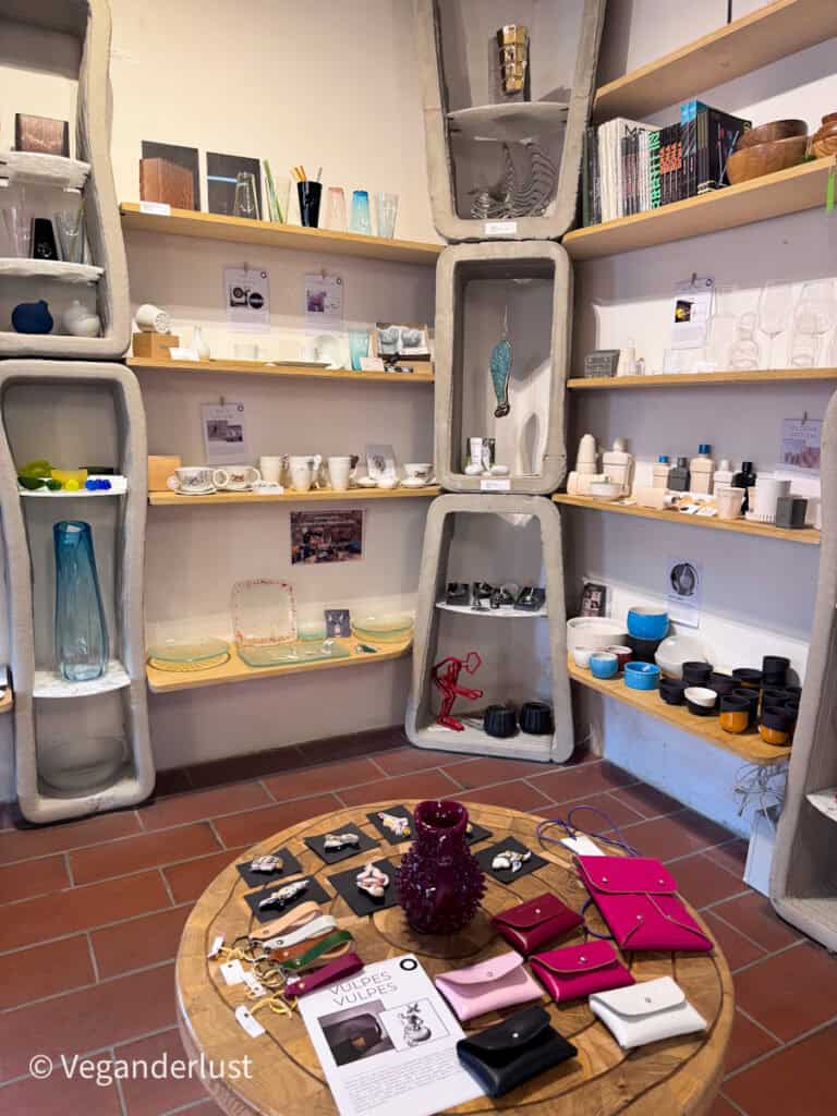 Small design shop in České Budějovice displaying handmade ceramics glassware books and colorful leather accessories on wooden shelves. A round table in the center shows small purses and jewelry highlighting local artisan crafts to browse while exploring things to do in České Budějovice.