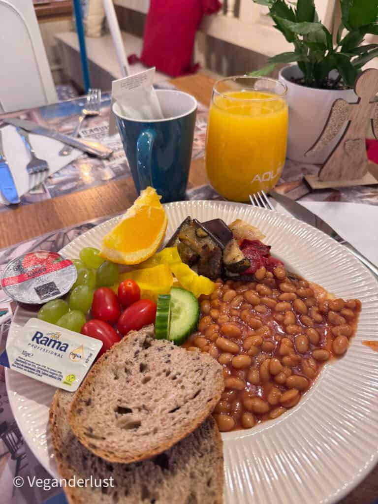 Breakfast plate with baked beans, roasted vegetables, bread, grapes, tomatoes, cucumber, and orange juice served at a cozy cafe table. Enjoying a relaxed breakfast before sightseeing is a great way to start a day exploring things to do in Cesky Krumlov.