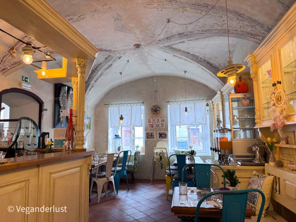 Charming cafe interior with vintage decor, pastel chairs, wooden tables, and soft lighting inside a historic building in Cesky Krumlov. Stopping for coffee or breakfast in cozy cafes is one of the relaxing things to do in Cesky Krumlov.