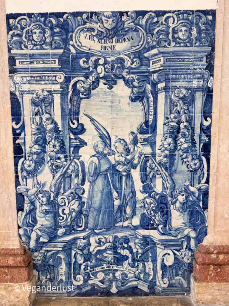 Blue and white ceramic tile mural showing detailed figures, decorative columns, and angels in an ornate scene. Text at the top reads "VIR ALEXO DE PENA FIRME" surrounded by intricate patterns and classical motifs.