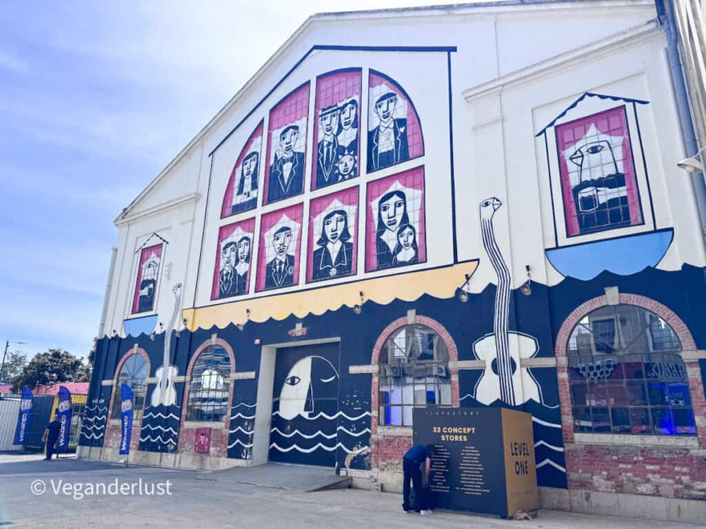 Large building facade decorated with graphic murals of people in window frames and oversized guitars along the bottom. A sign reads "33 CONCEPT STORES" and "LEVEL ONE" in front of this creative Lisbon space.