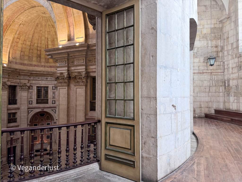 Open doorway leading to a curved balcony inside a domed church with stone walls and wooden flooring.